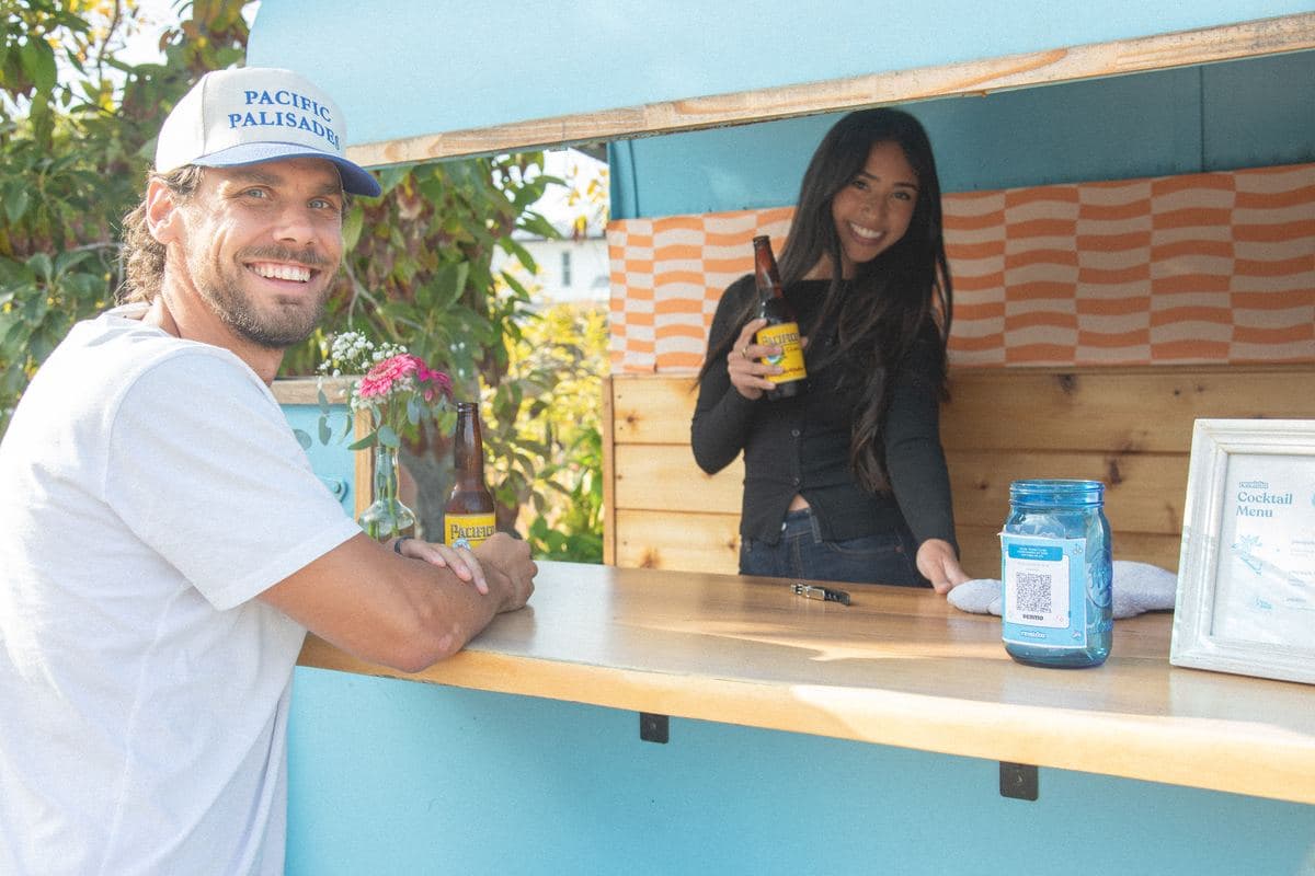 A guest and bartender cheersing with beers at the window