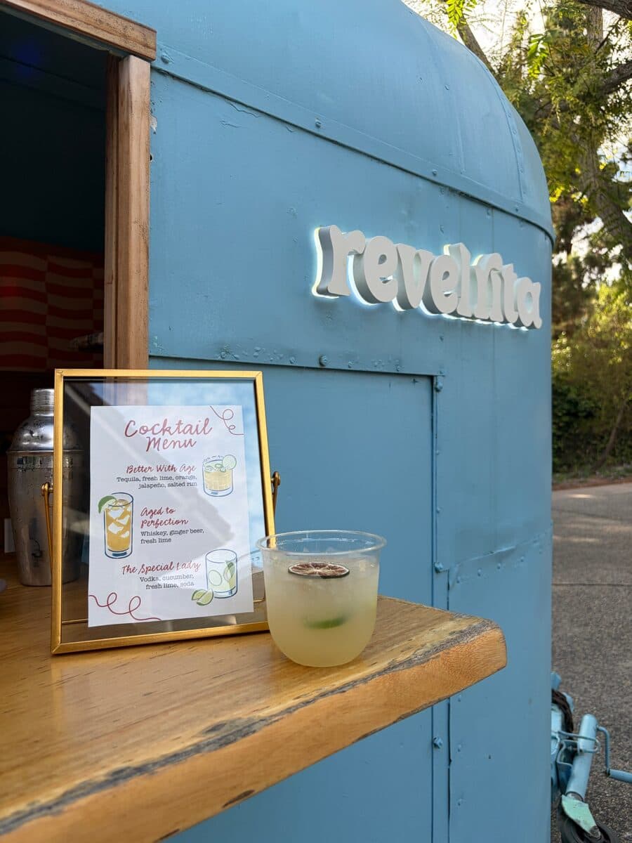 A framed cocktail menu and a margarita on the bar top under the lit sign