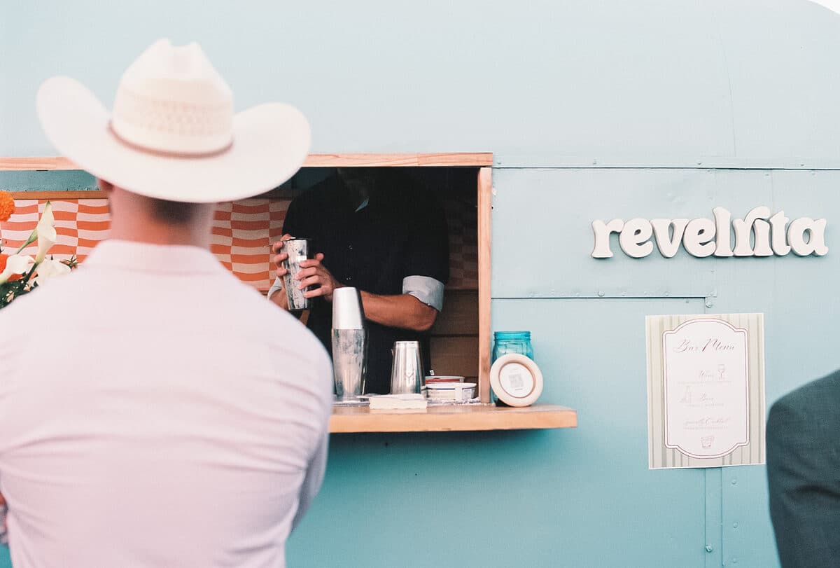 A guest in a cowboy hat watching the bartender shake a cocktail